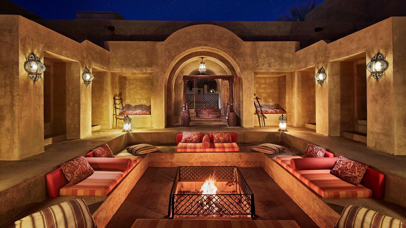 Desert resort sunken lounge with cushioned banquettes and lanterns around a lit fire pit at night