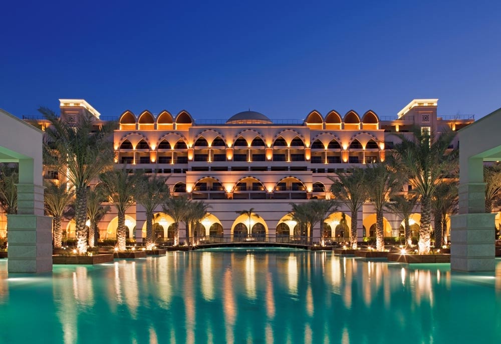 Arched palace-style resort facade lit at dusk and mirrored in a still lagoon pool